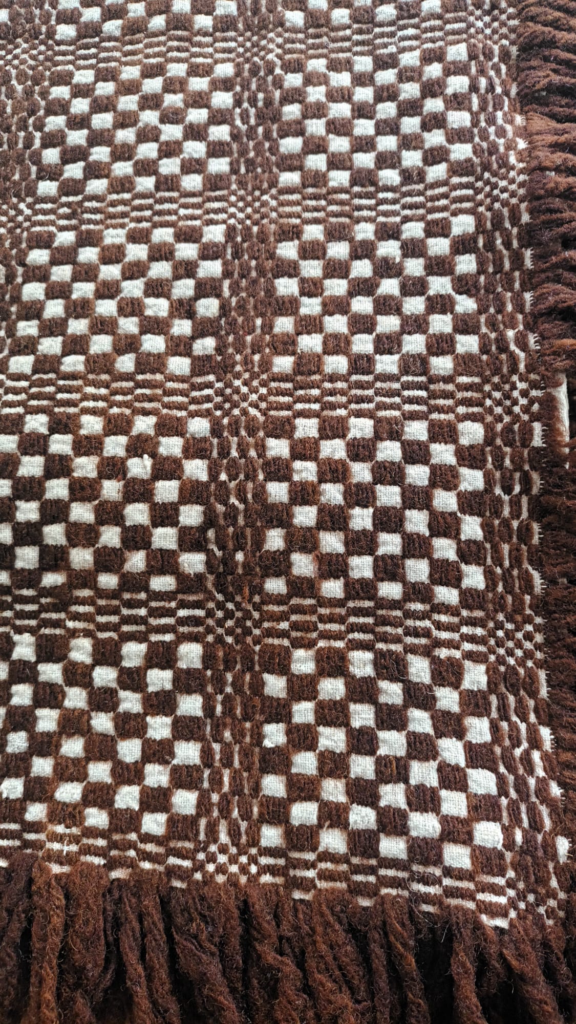 Pormenor de uma peça de lã castanha e branca com padrão geométrico e franja